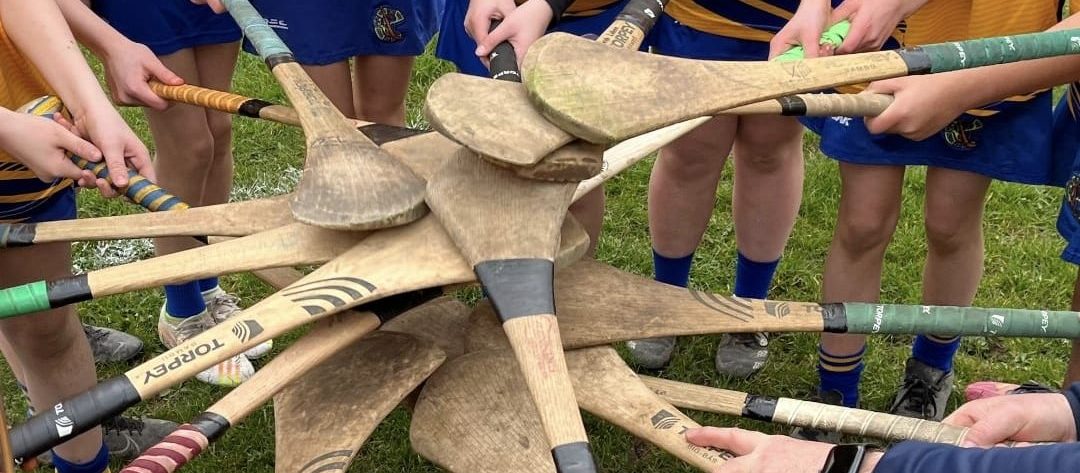 Camogie players stand in a circle, with their hurls touching in the centre